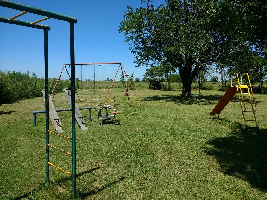 Parque de césped con hamacas, tobogán y otros juegos entre árboles.